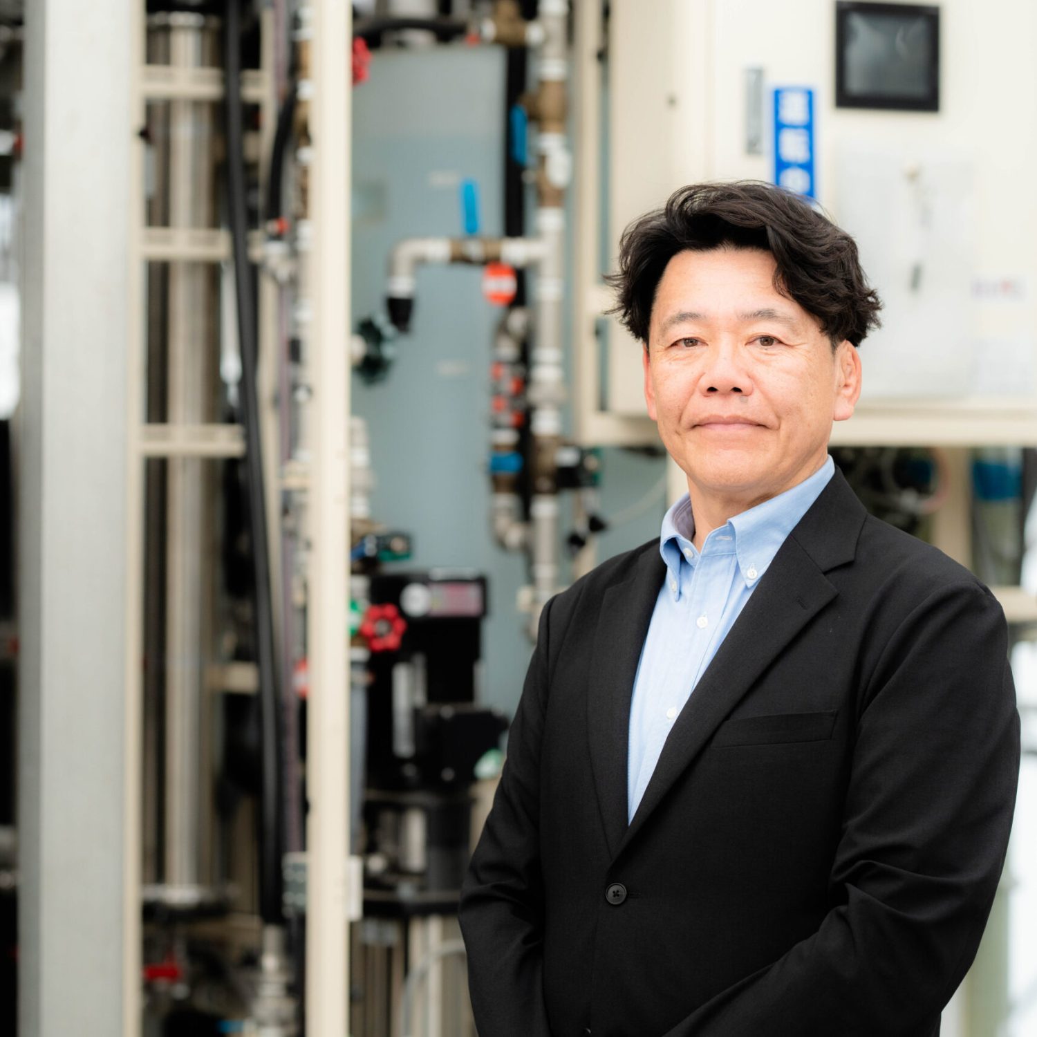 設備機器を背景に立つ株式会社渡邊企画 代表取締役 渡邊浩之
